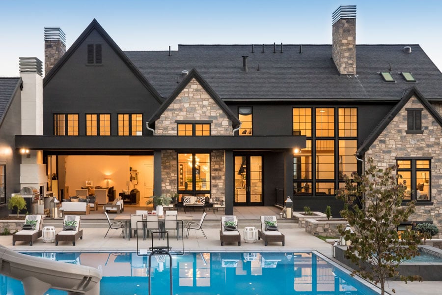 Back of house with pool and outdoor dining table at dusk. Large windows, modern home