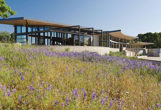A modern ranch that spreads horizontally across the top of a hill with large overhangs and walls made of glass.