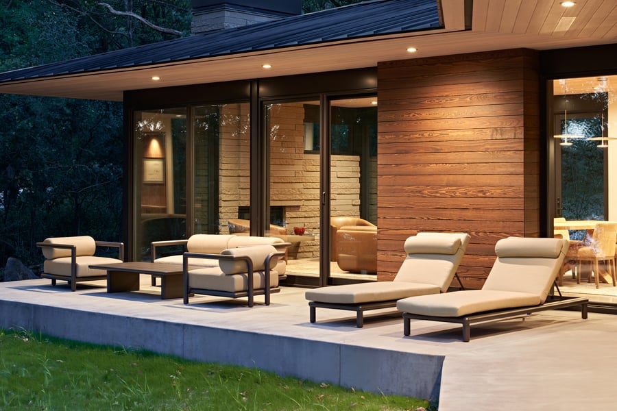 A patio with tan outdoor furniture, wood siding, and black E-Series gliding patio doors with dual-pane glass. 