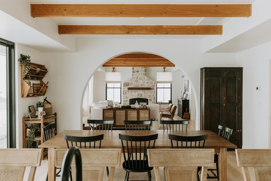 An arched doorway connects a kitchen with the family room beyond where a large stone fireplace is the central feature