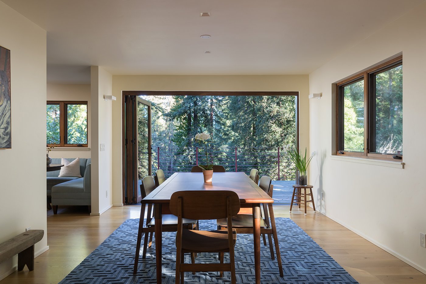 A dining room with casement windows on one side and a large, open bi-folding door at the end that is open to the deck outside.