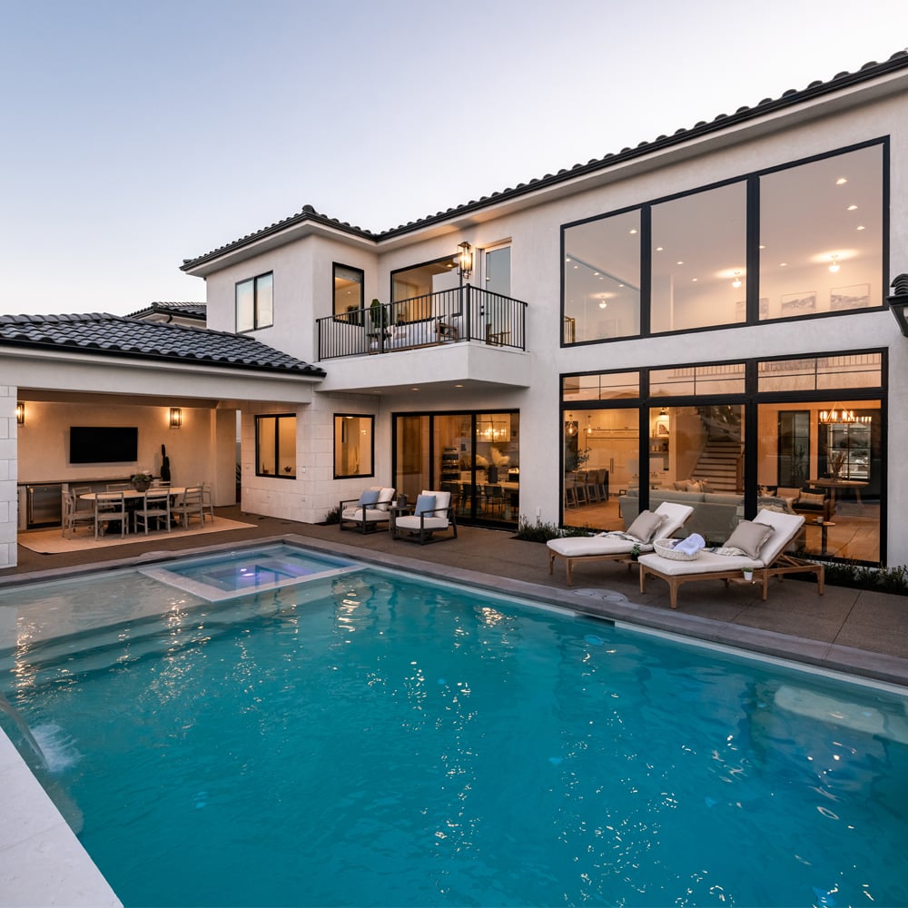 An outdoor dining area next to an underground pool with large, black windows and doors allowing deck access